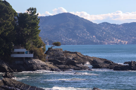 House surrounded by the trees on rocks stretching to the sea with cliffs and a mountain ridge in the distance on a sunny dayの写真素材