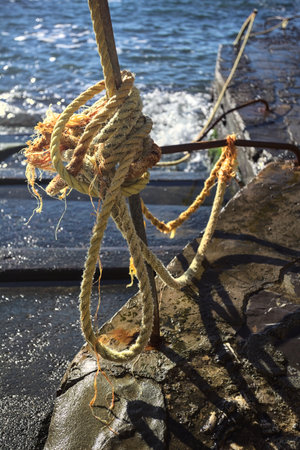 Yellow rope knotted on a pole by the edge of a staircase next to the sea on a sunny day with the sun...