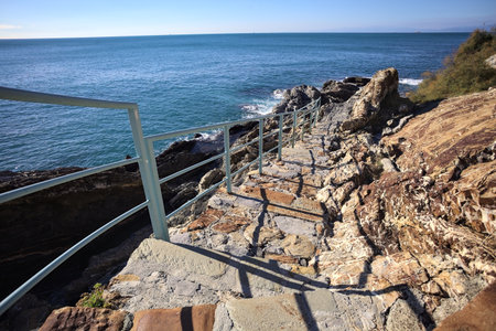 Descending staircase to the sea carved in a cliff bordered by an azure railing on a sunny dayの写真素材