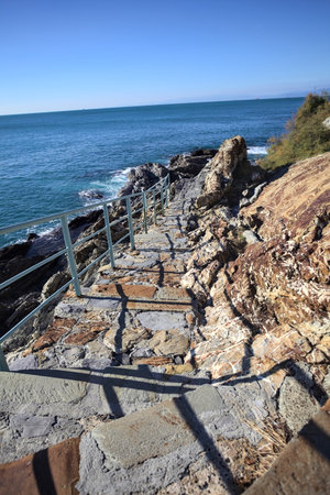 Descending staircase to the sea carved in a cliff bordered by an azure railing on a sunny day