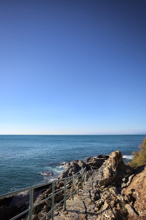 Descending staircase to the sea carved in a cliff bordered by an azure railing on a sunny dayの写真素材