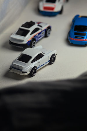 Mantua, Italy - 4TH JANUARY 2025 - Hot Wheels replicas of various Porsche cars, a 911 rallye, two 1996 Carrera, a 1971 911 and a 911 Carrera RS 2.7, on white board, bordered by white rolls of fabric, pretending to make a curve on a road and having a race のeditorial素材