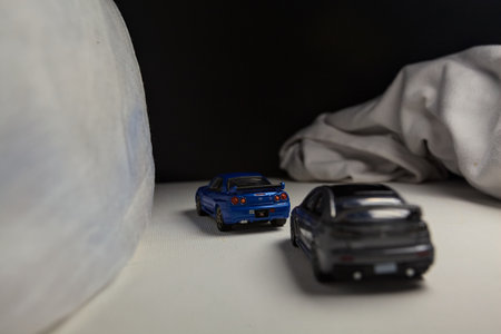 Mantua, Italy - 4TH JANUARY 2025 - Takara Tomy replicas of a Nissan Skyline GT-R V-Spec Nur II and a Mitsubishi Lancer Evolution on white board, bordered by white rolls of fabric, pretending to make a curve on a road and having a race between themのeditorial素材
