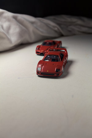 Mantua, Italy - 4TH JANUARY 2025 - Takara Tomy replicas of a Ferrari F40 and a Ferrari Enzo Ferrari on white board, bordered by white rolls of fabric, pretending to make a curve on a road and having a race between themのeditorial素材