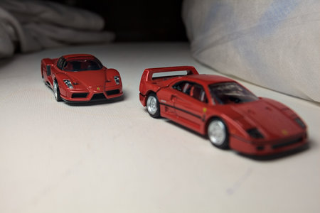 Mantua, Italy - 4TH JANUARY 2025 - Takara Tomy replicas of a Ferrari F40 and a Ferrari Enzo Ferrari on white board, bordered by white rolls of fabric, pretending to make a curve on a road and having a race between themのeditorial素材