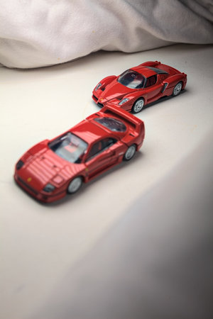 Mantua, Italy - 4TH JANUARY 2025 - Takara Tomy replicas of a Ferrari F40 and a Ferrari Enzo Ferrari on white board, bordered by white rolls of fabric, pretending to make a curve on a road and having a race between themのeditorial素材