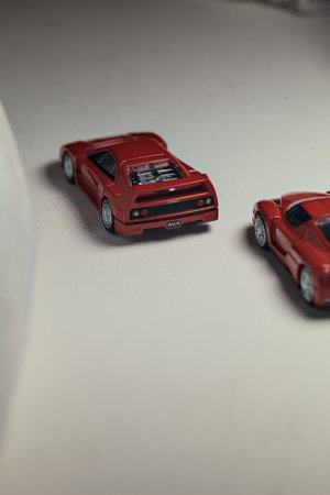 Mantua, Italy - 4TH JANUARY 2025 - Takara Tomy replicas of a Ferrari F40 and a Ferrari Enzo Ferrari on white board, bordered by white rolls of fabric, pretending to make a curve on a road and having a race between themのeditorial素材