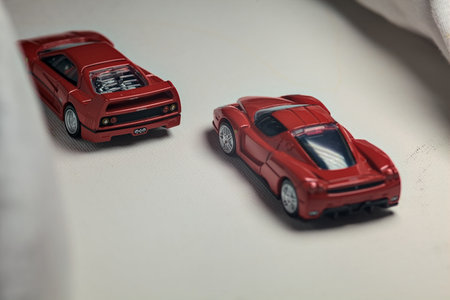 Mantua, Italy - 4TH JANUARY 2025 - Takara Tomy replicas of a Ferrari F40 and a Ferrari Enzo Ferrari on white board, bordered by white rolls of fabric, pretending to make a curve on a road and having a race between themのeditorial素材