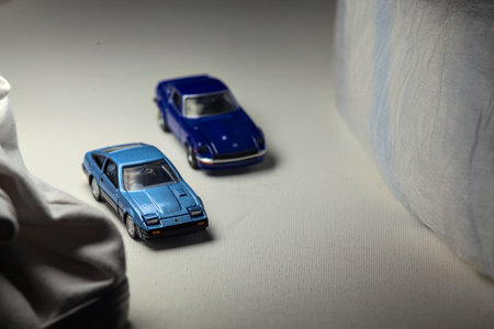 Mantua, Italy - 4TH JANUARY 2025 - Takara Tomy replicas of two Nissan Fairlady Z of different time periods on white board, bordered by white rolls of fabric, pretending to make a curve on a road and having a race between themのeditorial素材