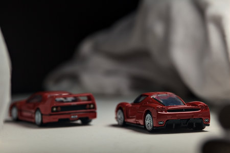 Mantua, Italy - 4TH JANUARY 2025 - Takara Tomy replicas of a Ferrari F40 and a Ferrari Enzo Ferrari on white board, bordered by white rolls of fabric, pretending to make a curve on a road and having a race between themのeditorial素材