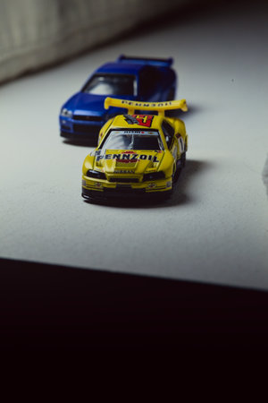 Mantua, Italy - 10TH JANUARY 2025 - Takara Tomy replicas of a Nissan Skyline GT-R V-Spec II Nur and a 1998 Nissan Skyline GT-R R33 in #23 Pennzoil Nismo yellow and black livery pretending to have a race, on a curve of a circuitのeditorial素材