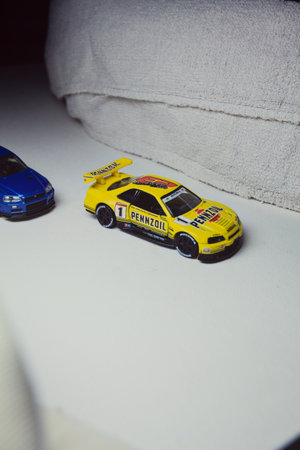 Mantua, Italy - 10TH JANUARY 2025 - Takara Tomy replicas of a Nissan Skyline GT-R V-Spec II Nur and a 1998 Nissan Skyline GT-R R33 in #23 Pennzoil Nismo yellow and black livery pretending to have a race, on a curve of a circuitのeditorial素材