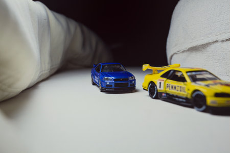 Mantua, Italy - 10TH JANUARY 2025 - Takara Tomy replicas of a Nissan Skyline GT-R V-Spec II Nur and a 1998 Nissan Skyline GT-R R33 in #23 Pennzoil Nismo yellow and black livery pretending to have a race, on a curve of a circuitのeditorial素材