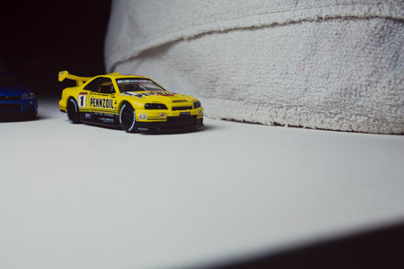 Mantua, Italy - 10TH JANUARY 2025 - Takara Tomy replicas of a Nissan Skyline GT-R V-Spec II Nur and a 1998 Nissan Skyline GT-R R33 in #23 Pennzoil Nismo yellow and black livery pretending to have a race, on a curve of a circuitのeditorial素材