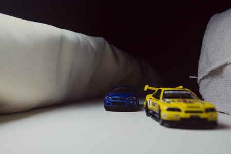 Mantua, Italy - 10TH JANUARY 2025 - Takara Tomy replicas of a Nissan Skyline GT-R V-Spec II Nur and a 1998 Nissan Skyline GT-R R33 in #23 Pennzoil Nismo yellow and black livery pretending to have a race, on a curve of a circuitのeditorial素材