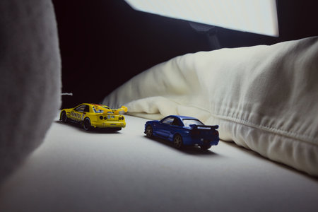 Mantua, Italy - 10TH JANUARY 2025 - Takara Tomy replicas of a Nissan Skyline GT-R V-Spec II Nur and a 1998 Nissan Skyline GT-R R33 in #23 Pennzoil Nismo yellow and black livery pretending to have a race, on a curve of a circuitのeditorial素材