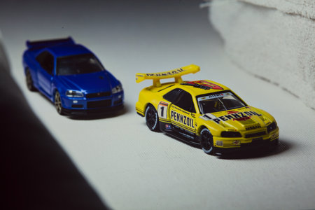 Mantua, Italy - 10TH JANUARY 2025 - Takara Tomy replicas of a Nissan Skyline GT-R V-Spec II Nur and a 1998 Nissan Skyline GT-R R33 in #23 Pennzoil Nismo yellow and black livery pretending to have a race, on a curve of a circuitのeditorial素材