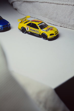 Mantua, Italy - 10TH JANUARY 2025 - Takara Tomy replicas of a Nissan Skyline GT-R V-Spec II Nur and a 1998 Nissan Skyline GT-R R33 in #23 Pennzoil Nismo yellow and black livery pretending to have a race, on a curve of a circuitのeditorial素材