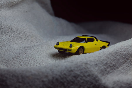 Mantua, Italy - 10TH JANUARY 2025 - Mini GT replica of a yellow Lancia Stratos HF Stradale pretending to run a rally on a snowy road, next to a cliff, in the mountainsのeditorial素材