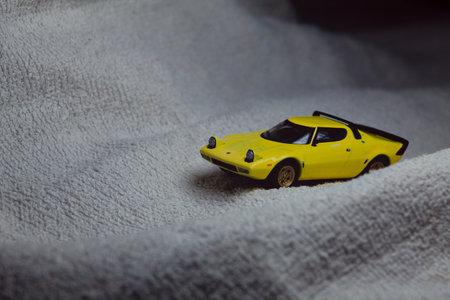 Mantua, Italy - 10TH JANUARY 2025 - Mini GT replica of a yellow Lancia Stratos HF Stradale pretending to run a rally on a snowy road, next to a cliff, in the mountainsのeditorial素材