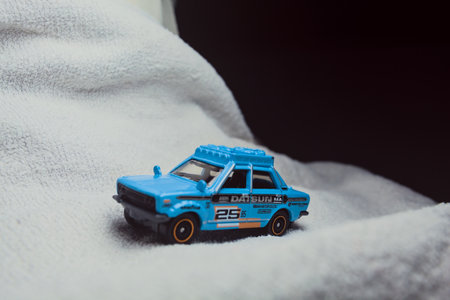 Mantua, Italy - 10TH JANUARY 2025 - Matchbox replica of a 1970 Datsun 510 in rally livery and trim pretending to run a rally on a snowy road, next to a cliff, in the mountainsのeditorial素材