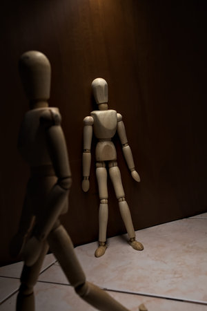 Wooden mannequin leaning against a wall with other wooden mannequins passing byの写真素材