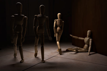 Wooden mannequin pretending to sit on a street and to lean on a wall raising his hand toward passing people with other wooden mannequins in the act of passing by on a streetの写真素材