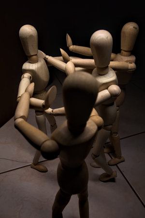 Wooden mannequin spreading its arms and standing against other three wooden mannequins pushing their...