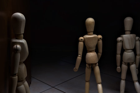 Wooden mannequin leaning against a wall pretending to watch and wait with other wooden mannequins in the act of passing by.の写真素材