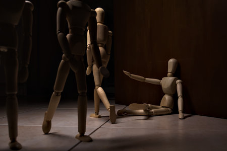 Wooden mannequin pretending to sit on a street and to lean on a wall raising his hand toward passing...