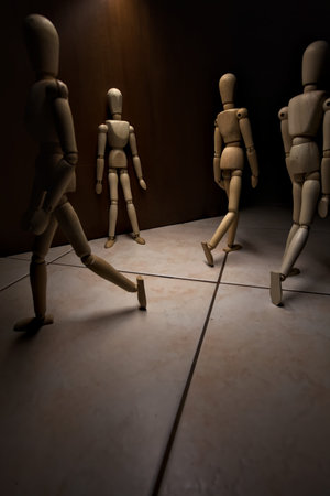 Wooden mannequin leaning against a wall pretending to watch and wait with other wooden mannequins in the act of passing byの写真素材