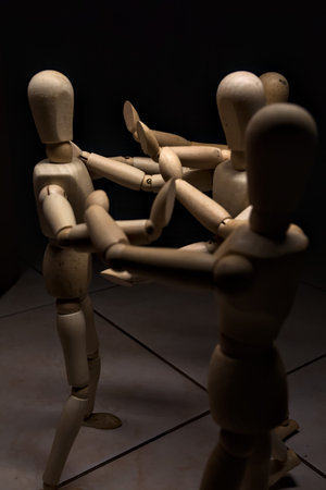 Wooden mannequin spreading its arms and standing against other three wooden mannequins pushing their...