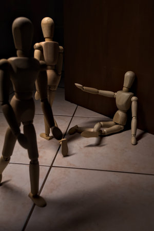 Wooden mannequin pretending to sit on a street and to lean on a wall raising his hand toward passing...