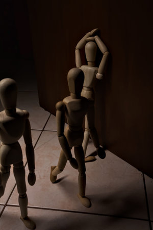Wooden mannequin leaning against and facing a wall with other wooden mannequins passing by on a...