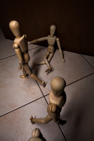 Wooden mannequin pretending to sit on a street and to lean on a wall raising his hand toward passing...