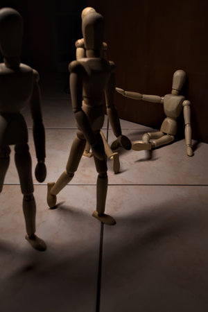 Wooden mannequin pretending to sit on a street and to lean on a wall raising his hand toward passing...