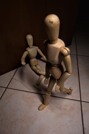Wooden mannequin pretending to sit on a street and to lean on a wall raising his hand toward passing people with other wooden mannequins in the act of passing by on a streetの写真素材