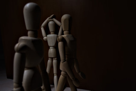 Wooden mannequin leaning against and facing a wall with its arms on its face with other wooden mannequins passing byの写真素材