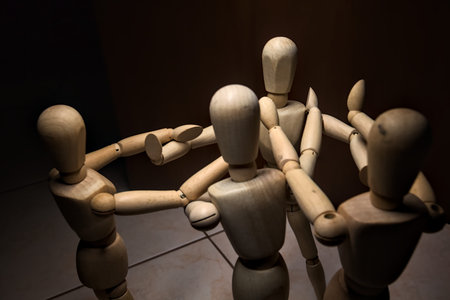 Wooden mannequin spreading its arms and standing against other three wooden mannequins pushing their arms against the one holding its place stillの写真素材
