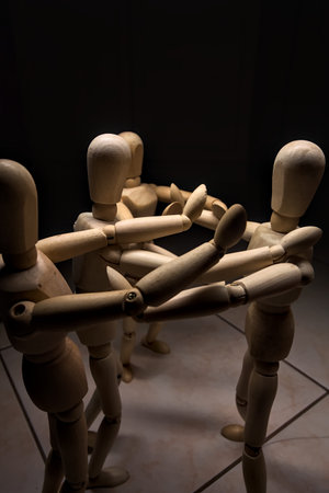 Wooden mannequin spreading its arms and standing against other three wooden mannequins pushing their arms against the one holding its place stillの写真素材