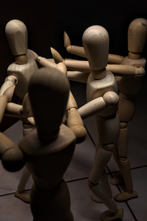 Wooden mannequin spreading its arms and standing against other three wooden mannequins pushing their arms against the one holding its place stillの写真素材
