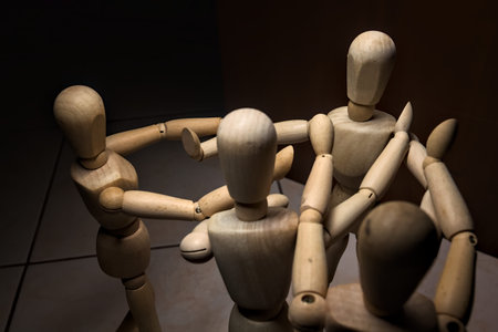 Wooden mannequin spreading its arms and standing against other three wooden mannequins pushing their arms against the one holding its place stillの写真素材
