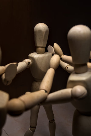 Wooden mannequin spreading its arms and standing against other three wooden mannequins pushing their arms against the one holding its place stillの写真素材