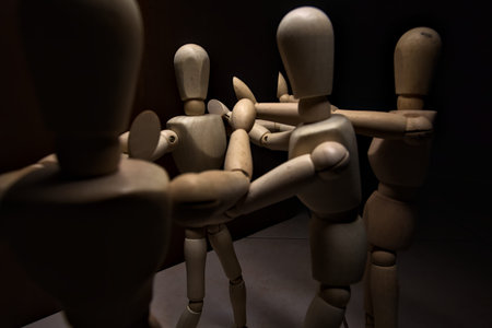 Wooden mannequin spreading its arms and standing against other three wooden mannequins pushing their arms againts the one holding its place stillの写真素材