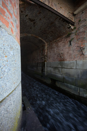 Closed sluices of a dam, with flowing water passing in a tunnel under a brick bridge