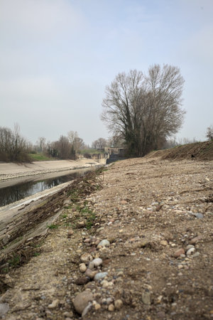 Diversionary channel with bare trees bordering the banks, reflected in the water together with the sky, on a cloudy dayの写真素材