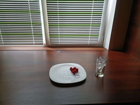 Strawberries on a beautiful white plate and a glass of ice next to itの写真素材