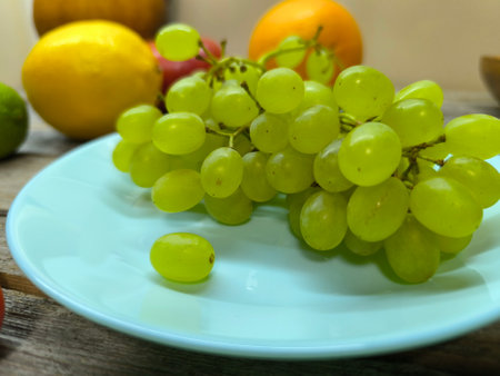green grapes on a turquoise plate surrounded by fruits.の写真素材