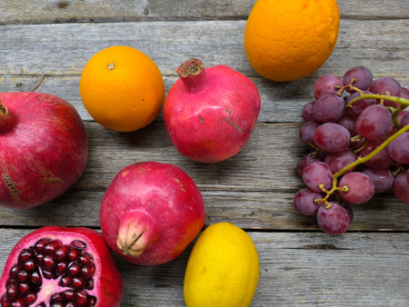 Sweet red pomegranate, oranges and red grapes arranged on a wooden table, top viewの写真素材