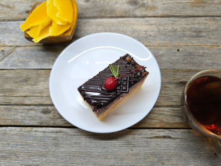 Chocolate cake with cherries lies on a white plate next to a cup of teaの写真素材